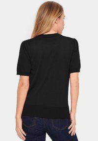 Black short-sleeve sweater made of smooth knit fabric, featuring a ribbed waistband and puffed shoulder details. Worn with dark jeans.