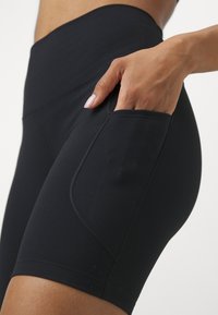 Pantalones cortos de ciclista negros de tiro alto hechos de tela elástica, con un bolsillo lateral, costuras planas y un diseño ceñido que llega hasta la mitad del muslo.