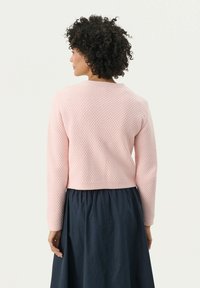 Light pink textured sweater with a round neckline and long sleeves, cropped length, worn over a dark blue skirt.