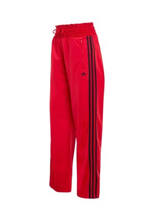 Červené sportovní kalhoty s černými trojitými pruhy po stranách, pružným pasem se stahovací šňůrkou a kapsou na boku se zipem.