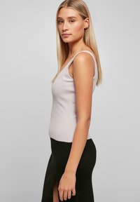 Licht lavendelkleurig geribd tanktop met dunne banden, benadrukt door een aansluitend ontwerp. Draagt met een zwarte rok tot de knie met een zijsplit.