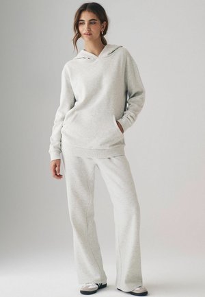 Hellgrauer Hoodie mit Kängurutasche und passenden weit geschnittenen Sweatpants. Weicher Stoff mit gerippten Bündchen, versehen mit dezenten Nähdetails.