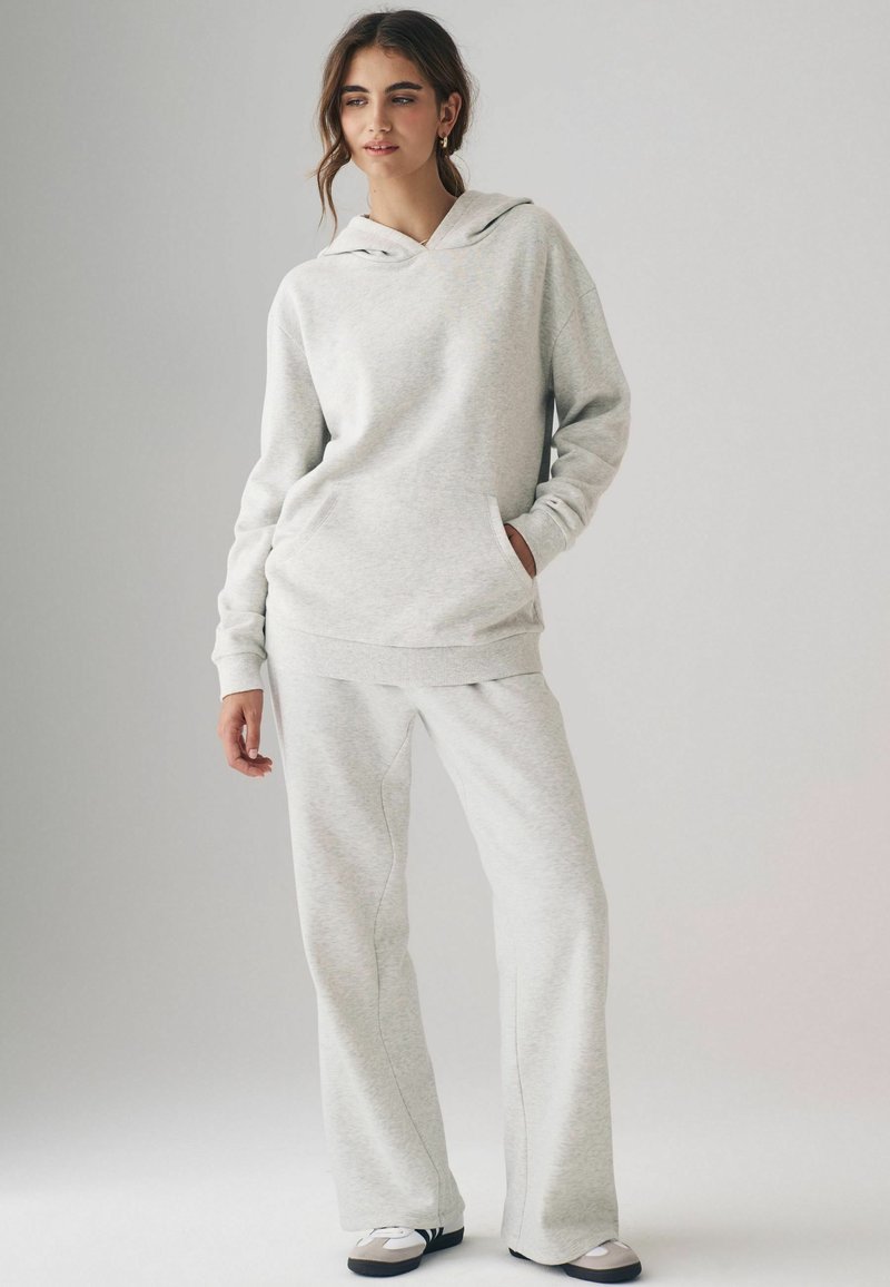 Hellgrauer Hoodie mit Kängurutasche und passenden weit geschnittenen Sweatpants. Weicher Stoff mit gerippten Bündchen, versehen mit dezenten Nähdetails.