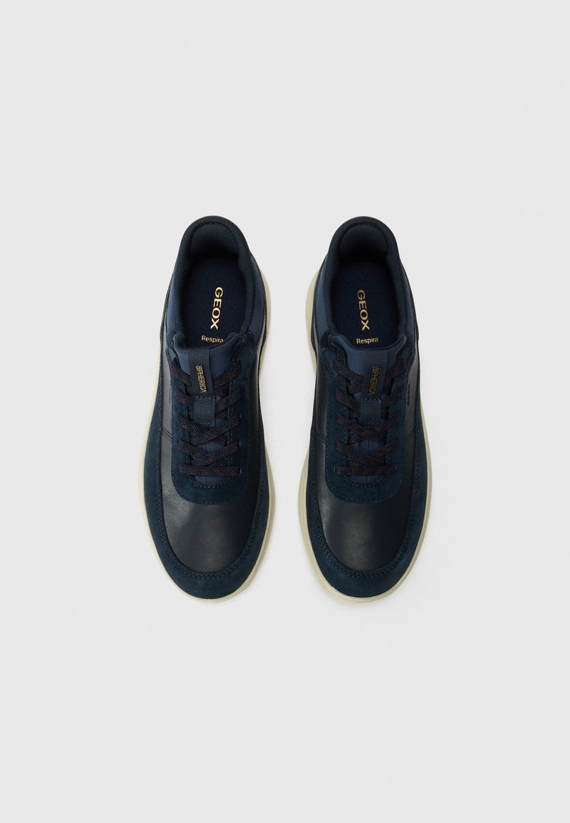 Zapatillas de deporte de un oscuro color marino, hechas de cuero y textil con una textura suave, cordones en contraste, suela color crema y un detalle de logo dorado.