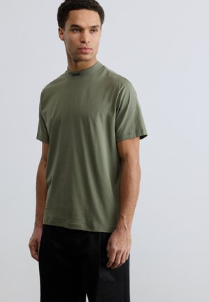Olive green short-sleeve t-shirt with a high collar and black logo text. Made of smooth fabric, featuring a relaxed fit and minimal seams.