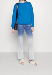 Ljusblå sweatshirt med rund halsringning, matchad med ljusblå utsvängda jeans med en graderingseffekt. Vita tofflor i päls.