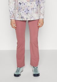 Pantalons roses extensibles avec une coupe droite, associés à des chaussures de randonnée bleu clair avec des semelles noires et des lacets noirs. Haut à manches longues coloré.