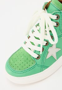 Groene hoge sneakers van leer en suede, met witte veters, geperforeerde neus en een witte steraccent aan de zijkant.