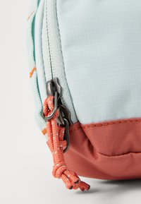 Helles blaues Täschchen mit strukturierter Oberfläche, orangen Akzenten und einem zweifarbigen Design. Hat einen Reißverschluss mit metallischen Beschlägen und einem geflochtenen Zugband.