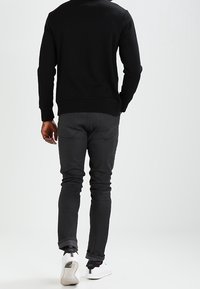 Sudadera negra con dobladillo acanalado, combinada con jeans ajustados gris oscuro y zapatillas blancas. La vista muestra la parte posterior del atuendo.