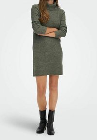 Abito a maglia verde oliva con colletto alto, maniche lunghe, orlo e polsini a costine, abbinato a stivali al ginocchio in pelle nera.