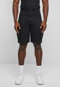 Shorts cargo noirs avec un devant plat, des poches latérales et une coupe droite. Fabriqués en tissu durable, complétés par des baskets blanches et des chaussettes.