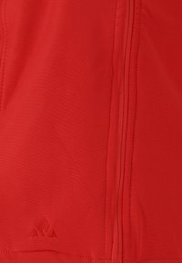 Tissu rouge avec une fermeture éclair verticale et un petit logo triangulaire brodé près du coin inférieur gauche.