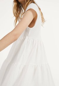 Vit texturerad klänning med en åtsittande bodice och korta ärmar, med en lager-på-lager, utsvängd kjol och en rund halsringning.