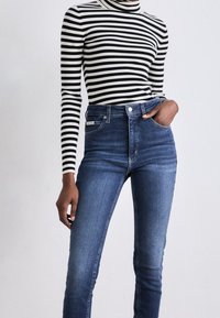 Svart och vit randig polotröja i kombination med högmidjade, blå denimjeans. Slim fit-design, mjuk textur och minimal detaljering.