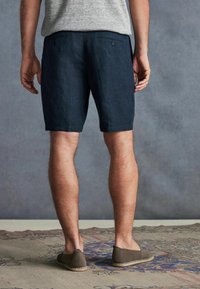 Pantalonii scurți din in de culoare bleumarin au o croială lejeră, două buzunare la spate și o suprafață ușor texturată, asortați cu o pereche de pantofi slip-on waveni maro.