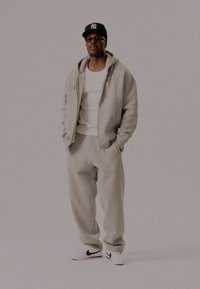 Lys grå hettegenser og joggebukser laget av mykt stoff, sammen med en hvit t-skjorte og hvite sneakers med en svart logo.