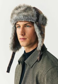 Pruunist ruudulise mustriga müts, millel on hall sünteetiline karusnahk, kõrvahood ja pruun nahk. Kanda koos tekstuuriga halli jope ja musta sviitriga.