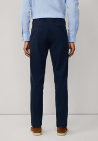 Navy blue trousers with a slim fit, made of smooth fabric. Features two back pockets with button closures. Worn with a light blue shirt.