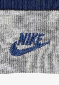 Pilkas audinys su raštuota tekstūra, kuris turi tamsiai mėlyną siuvinėtą "Nike" logotipą ir swoosh dizainą.