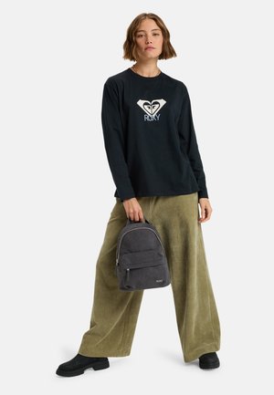 Zwarte lange mouw shirt met een witte Roxy-logo, gecombineerd met olijfgroene corduroy wijde broek en een kleine grijze rugzak. Zwarte laarzen.