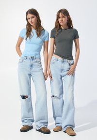 T-shirt fitted blu chiaro e grigio scuro, abbinati a jeans a gamba larga blu chiaro strappati e scarpe slip-on marroni.