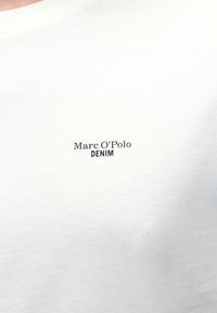 Material alb cu text mic negru „Marc O'Polo DENIM” imprimat la nivelul pieptului.
