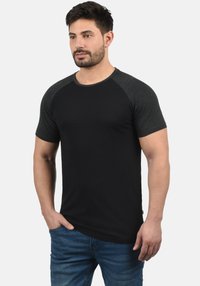 T-shirt nera con maniche raglan corte in grigio scuro, realizzata in tessuto morbido. Presenta un design classico con scollo a girocollo e una vestibilità comoda.