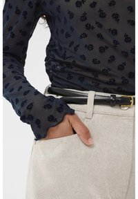 Navy sheer top met bloemmotief, lange mouwen met gerimpelde manchetten, gecombineerd met beige broek en een zwarte riem met een gouden gesp.