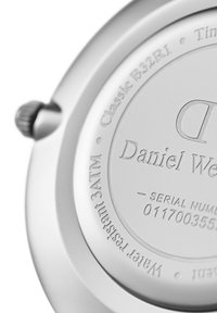 Round silver watch back with engraved text including brand name, model, serial number, and water resistance details. Polished metal finish.