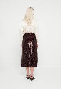 Jupe midi en sequins marron avec une coupe droite. Fermeture zippée au dos et fente latérale. Associée à une chemise blanche à manches longues.