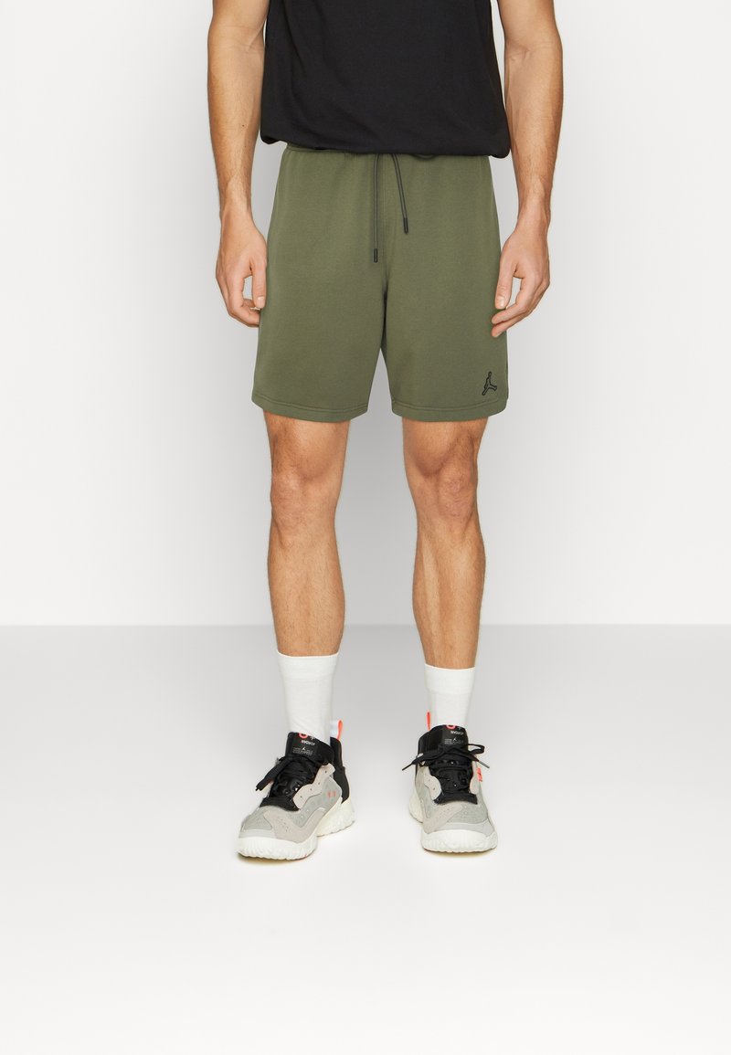 Shorts verts avec taille élastique et cordon de serrage, dotés de poches latérales et d'un petit logo noir. Portés avec des baskets noires et des chaussettes blanches.