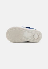 Adidași albaștri cu partea superioară din țesătură texturată, talpă din cauciuc alb și model de tăietoare în zigzag. Prezintă două curele velcro pentru închidere.