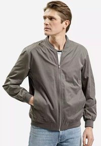 Szary bomber jacket z zamkiem z przodu, elastycznymi mankietami i pasem. Gładka tekstura, standardowy krój, noszony na pasiastej koszuli.