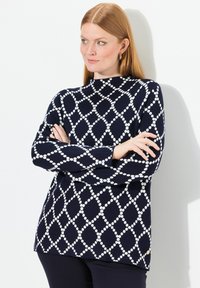 Maglione blu navy con motivo geometrico bianco, caratterizzato da un collo alto, maniche lunghe e una vestibilità morbida. Tessuto a maglia morbida.