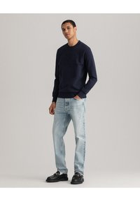 Mörkblå sweatshirt med präglad logotyp, långa ärmar och ribbade ärmslut. Kombinerad med ljusblå jeans och svarta skor. Enkel, modern design.