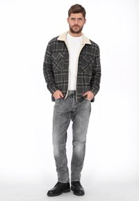 Camisa de franela de manga larga en gris oscuro con cuadros rojos y blancos, con un cuello de pana sintética en color crema, combinada con vaqueros grises y botas negras.