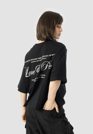 Black oversized cotton t-shirt featuring white text on the back, short sleeves, and a relaxed fit. Paired with black cargo pants.
