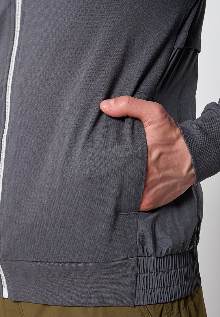 Giacca grigia con zip, dal tessuto liscio, con tasca laterale, vita elasticizzata e tessuto contrastante nella parte inferiore.
