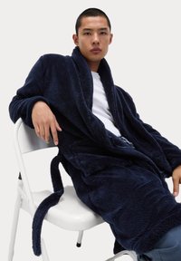 Granatowy, pluszowy szlafrok z długimi rękawami i kołnierzem szalowym, z wiązaniem w pasie i bocznymi kieszeniami. Gładka tekstura, luźny krój.