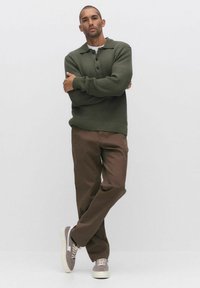 Olijfgroene geribde trui met een kraag, drie knopen, gedragen met bruine rechte broek en grijze sneakers met witte zolen.
