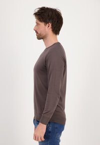 Maglione grigio a manica lunga con collo a giro, realizzato in tessuto morbido. Presenta polsini e orlo a coste, con una vestibilità casual. Senza loghi visibili.