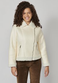 Krém színű műszőrme dzseki steppelt mintával, lehajtható gallérral és cipzáros zsebekkel. Shearling díszítéssel a mandzsettákon és az alján.