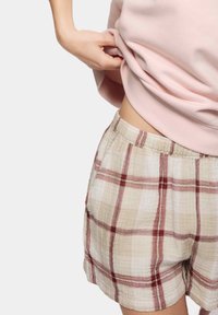 Gevlochten shorts in beige en lichtrood met een elastische tailleband. De stof lijkt zacht en lichtgewicht, met een losse pasvorm.
