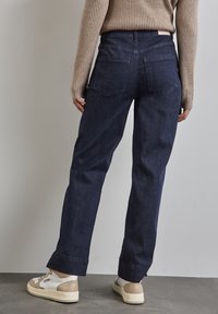 Jean en denim bleu foncé avec taille haute, coupe décontractée et ourlets retroussés ; il possède deux poches arrière et des détails de couture minimaux.