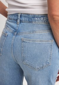 Ljusblå denimjeans med hög midja, som har två bakfickor och en synlig NA-KD-logotyp på midjebandet. Strukturerad yta och sömnadsdetaljer.