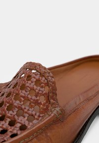 Chaussure à enfiler en cuir marron avec un motif tissé sur la partie supérieure, une texture lisse et une semelle flexible. L'intérieur est légèrement rembourré.