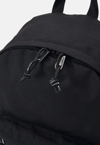 Sac à dos noir en tissu texturé, avec des cordons de serrage noirs réglables et des accents en métal au niveau de la fermeture et de la poche.