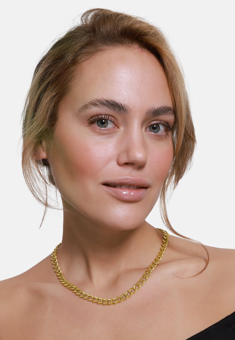 Collier en métal doré avec des maillons entrelacés, affichant une texture lisse et une largeur substantielle, porté à la base du cou.