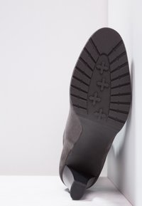 Bottine en daim gris avec un bout pointu et une semelle en caoutchouc noire, présentant un motif antidérapant et un talon modeste.